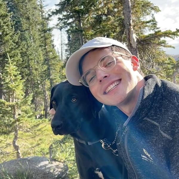 Picture of Alex outdoors with his dog who is a black dog