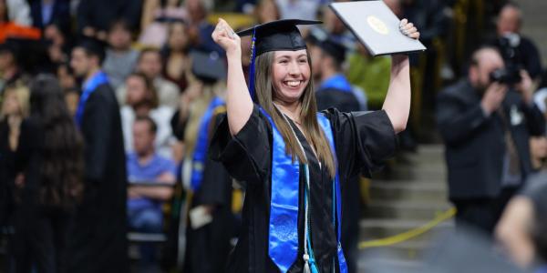 Woman cheers while holding diploma cover