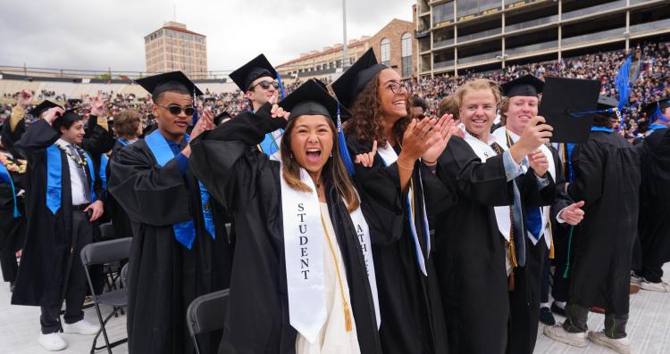 Students in regalia cheer during commencement