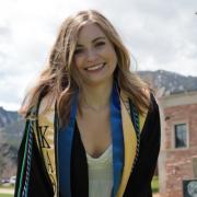 Olivia in her graduation regalia outside the Koelbel Building.