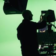 Silhouette of people against a green screen. Recording equipment is visible in the foreground.