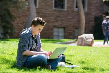student on computer in the grass