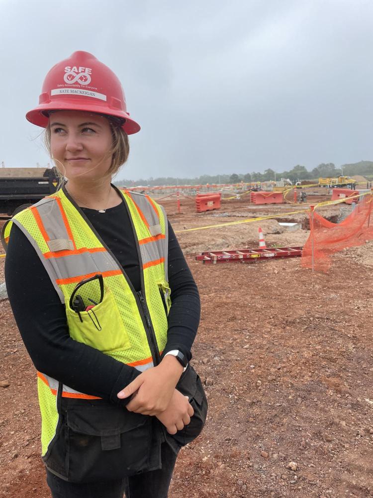 Kate MacKeigan in a hard hat and construction vest on a construction site.