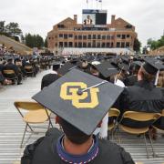 A graduation ceremony from the back with CU on a student's cap in the foreground.