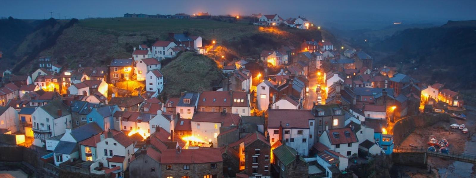 Houses all lit up in a small English village at night.