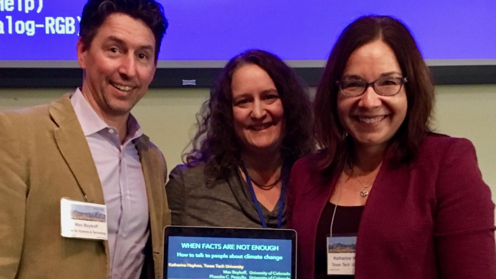 Three professors smiling holding a laptop with a presentation on Climate Communication