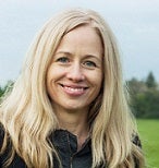 Woman smiling with blond hair, grass and trees in the background