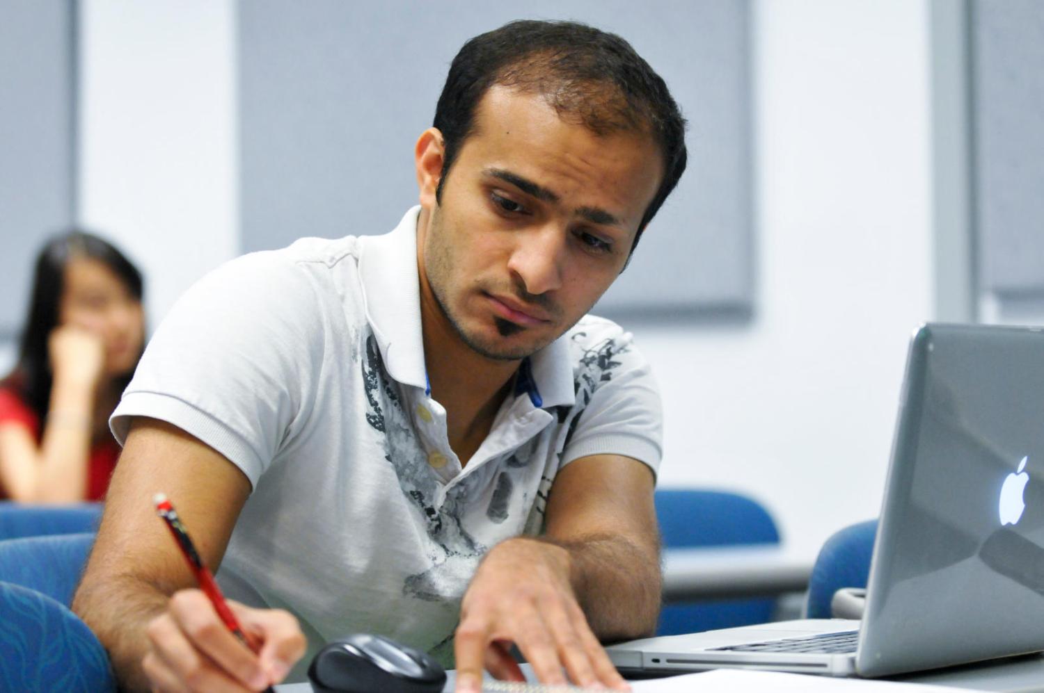 Student holding a pen and writing in front of a computer