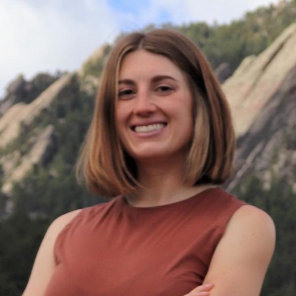 Staff member standing with arms folded in from of mountains and blue sky