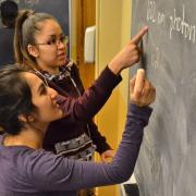 Two students work a chemistry problem at a blackboard