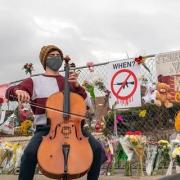 Celloist playing in front of memorial (fence with signs, flowers) from the Boulder Shooting incident in March 2021