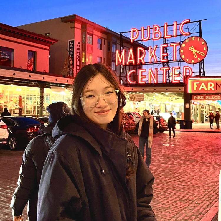 Krista Phommatha at night in front of a lit sign that says "Public Market Center"