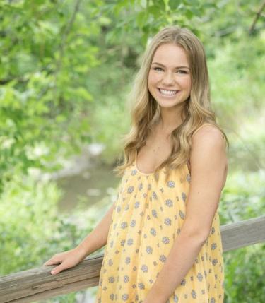 Nichole Loomis in a summery dress on a bridge in front of trees.