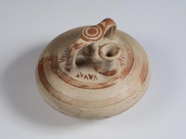 Photograph of stirrup jar, tan with reddish-brown slip decoration, from high angle against neutral gray background.