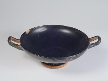 Photograph of a black-gloss kylix, from a high angle against a neutral gray background.