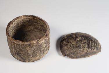 Photograph of cylindrical pyxis and lid, side-by-side from high angle against neutral gray background.