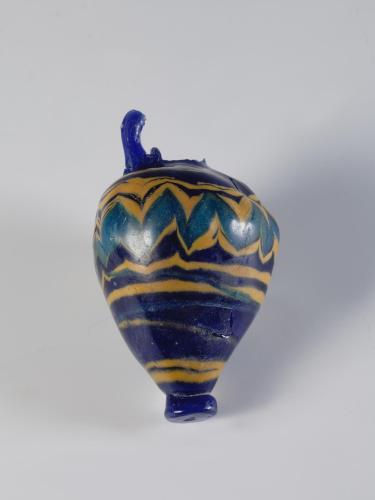 Photograph of a broken multi-colored glass vase with an ovoid body that tapers to a narrow, flat base. Neck and most of handle broken. From the side against a neutral gray background.