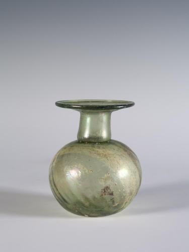 Photograph of a clear glass vessel with a round body and a relatively short neck that tapers into a horizontal, disk-shaped mouth, from the side against a neutral gray background.