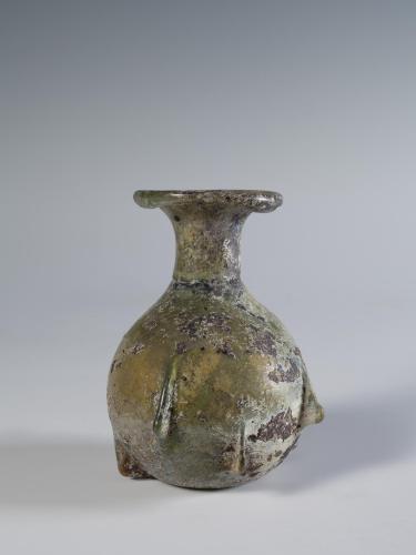 Photograph of a glass vessel with a round body and relatively short neck that flares into a horizontal, disk-shaped mouth, from the side against a neutral gray background.
