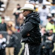 Coach Prime walks the sidelines during a snowy football game.