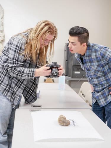Students gathered around a camera reviewing a photo of fossil. 
