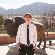 Elijah Boykoff on the CASE building roof. A buffalo statue is in the background with moutains in the distance.