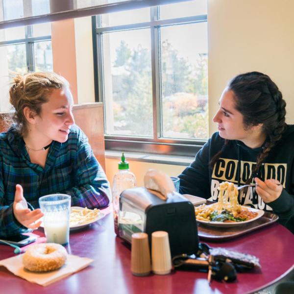 Two female students sitting at a table and eating lunch in the C4C dining center