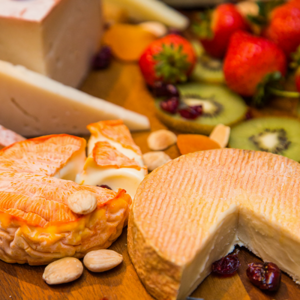 Several cheeses and fruits on wood board