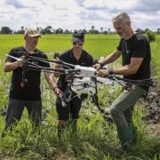 Three operators work on a drone in the middle of a grassy field. 