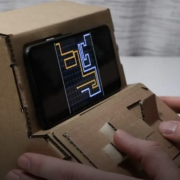 Two people play on tiny arcades made out of cardboard