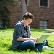 A student works on a laptop while sitting outdoors