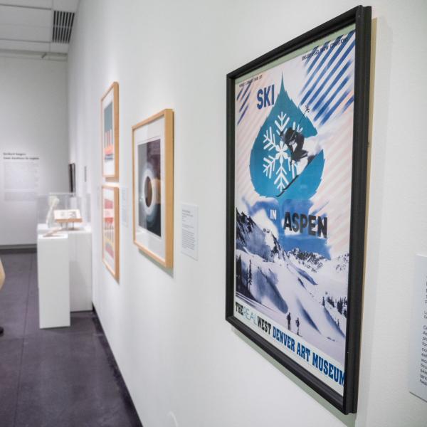 Installation shot of "Herbert Bayer: From Bauhaus to Aspen." A corner of the C-U Art Museum featuring many framed artworks hanging on the walls or resting on pedestals.