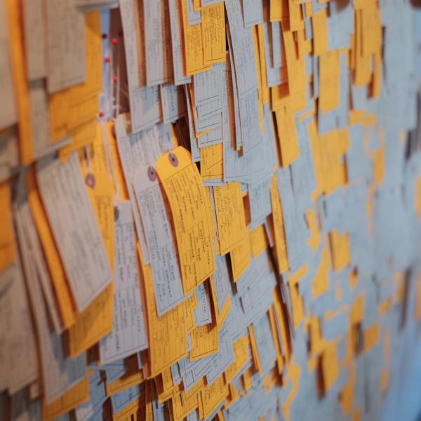Detail of installation shot of "Hostile Terrain 94". Many orange and beige tags hang from a wall.