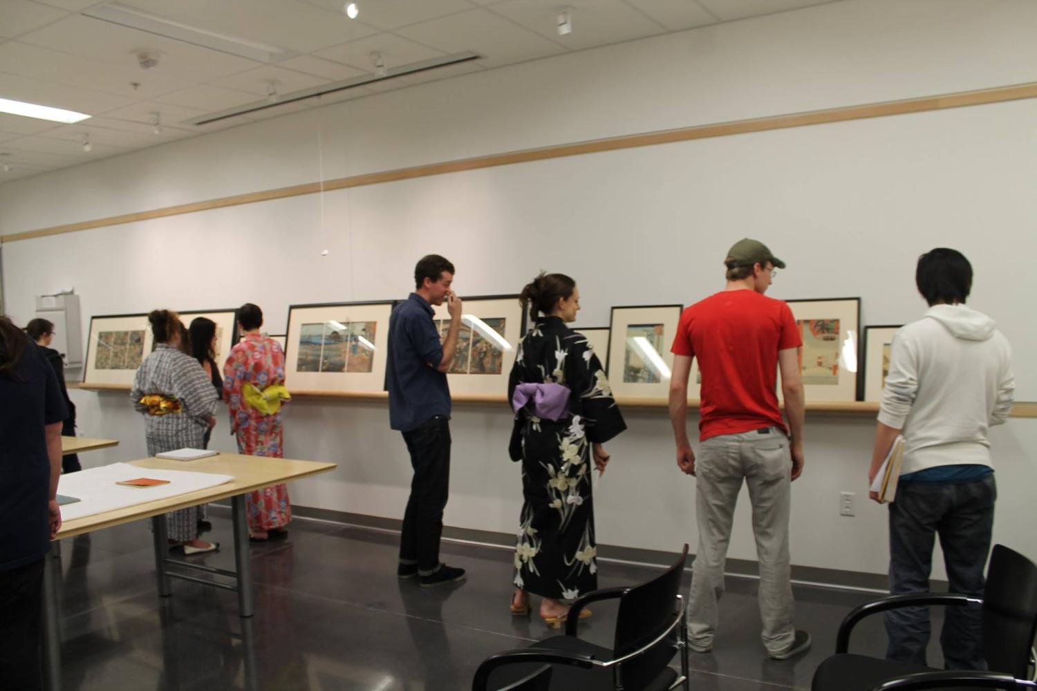Students view framed prints on a wall.