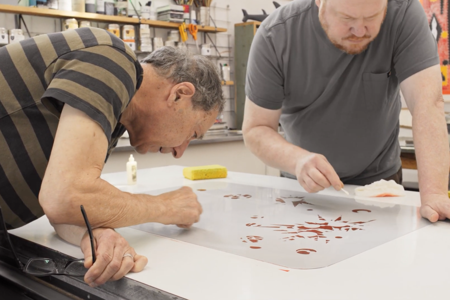Bud Shark and his studio assistant, Evan Colbert, leaning over a lithograph print with swabs as they carefully edit it.