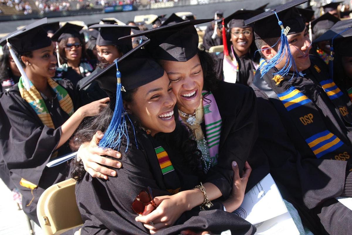 students in grad regalia hugging each other and smiling during commencement