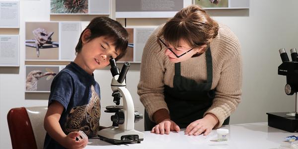 Student showing microscope to young child