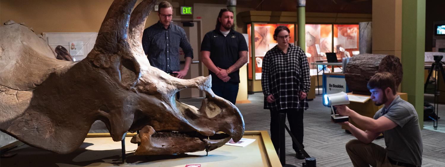 students gathered around triceratops skull in the paleontology hall