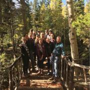 Mike breed with students on a wooded bridge. Aspen trees in background, the class is on a hike