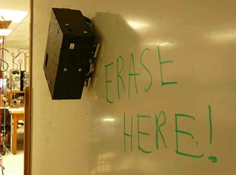 The Eraser-Bot sits poised to erase the words "Erase Here!" on a whiteboard