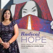 Photo of Noreen Naseem Rodríguez standing infront of a wall mural painting.