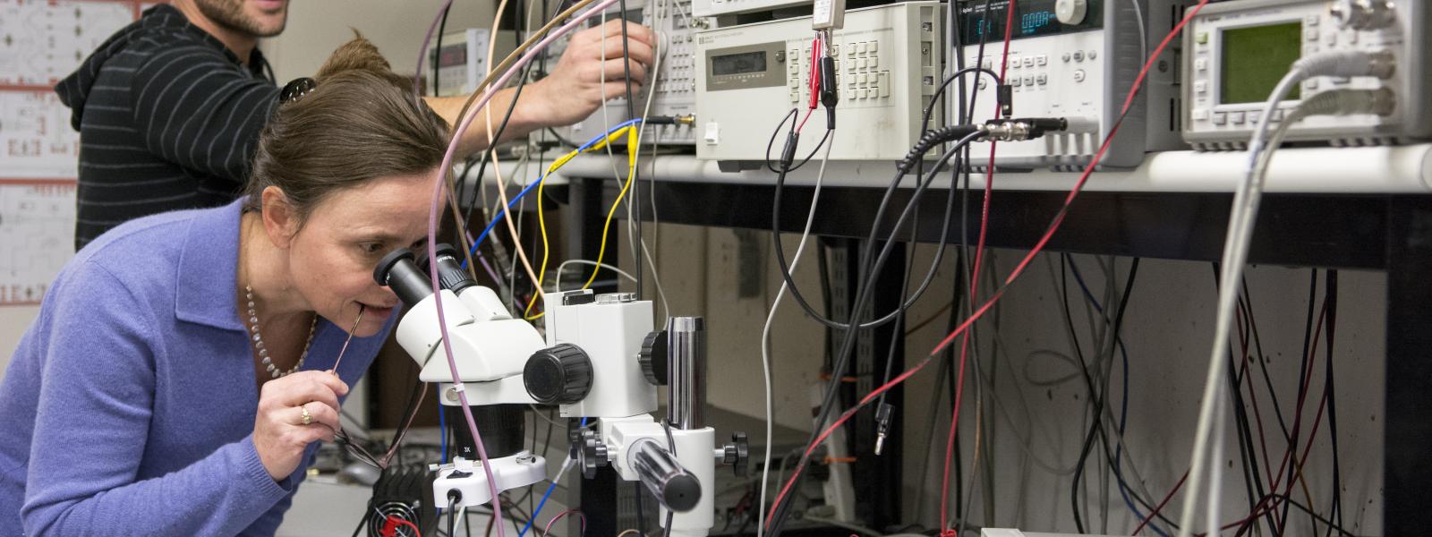 Zoya Popovic looks into a microscope in her lab as a grad student looks on