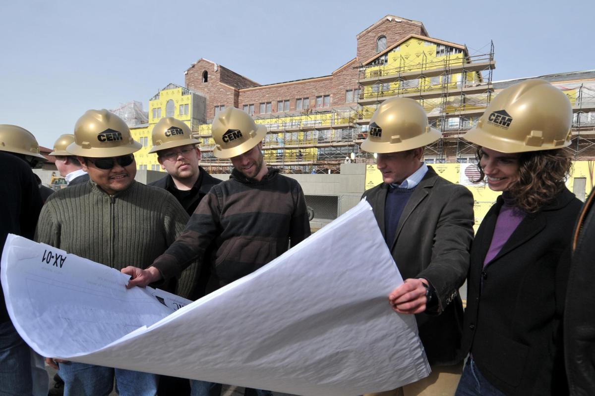 A group of construction engineers looks at blueprints outside a campus building under construction