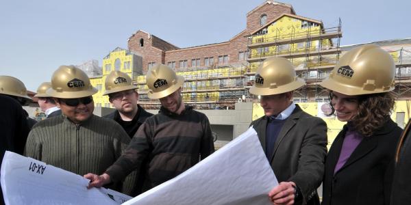 A group of construction engineers looks at blueprints outside a campus building under construction