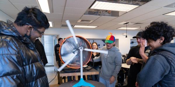 A Wind Team member in a colorful propeller beanie operates a model turbine at an outreach event