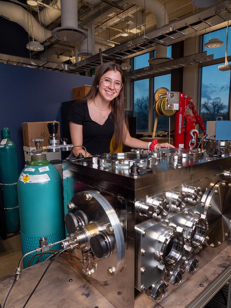 Female CU Boulder engineering PhD student, smiling at camera, seen working in a college lab. 