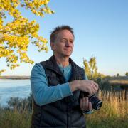 Kent with his camera by a lake with fall trees 