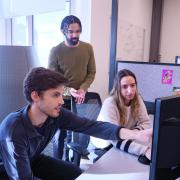 Three graduate students discuss a project in their office space