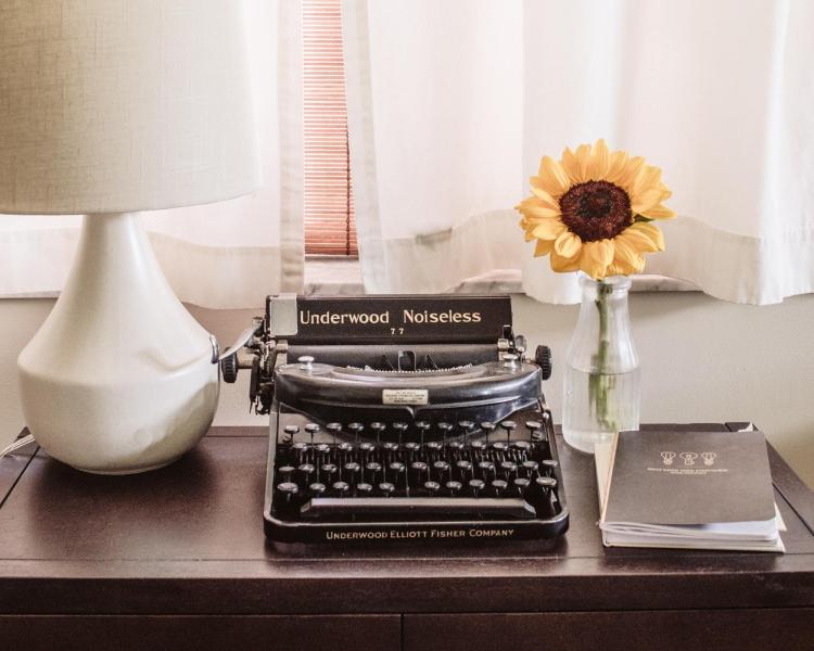 A typewriter on a desk next to flowers