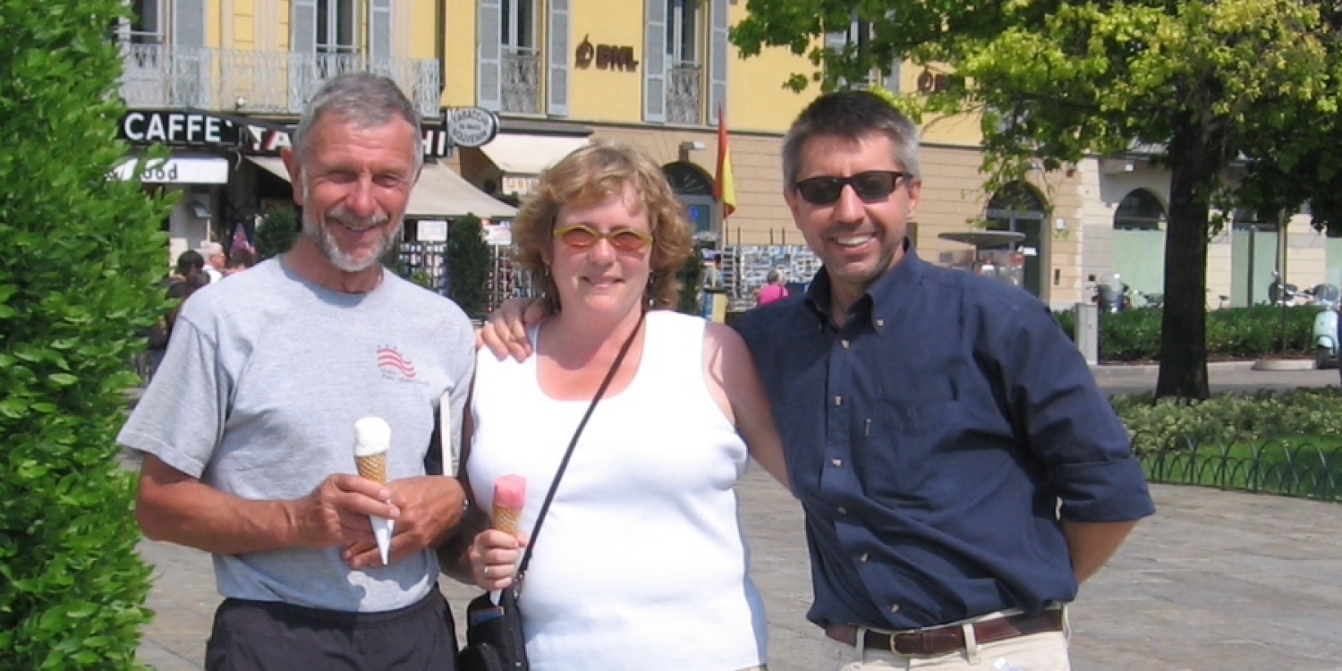 2 men and a woman holding ice creams cones, posing in a European town square.